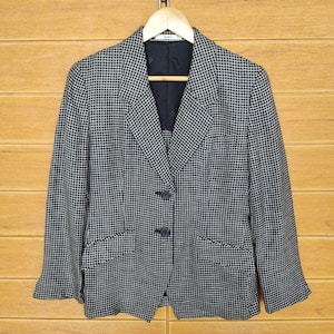 May include: A black and white checkered blazer with a button closure. The blazer has a notched collar and two flap pockets.