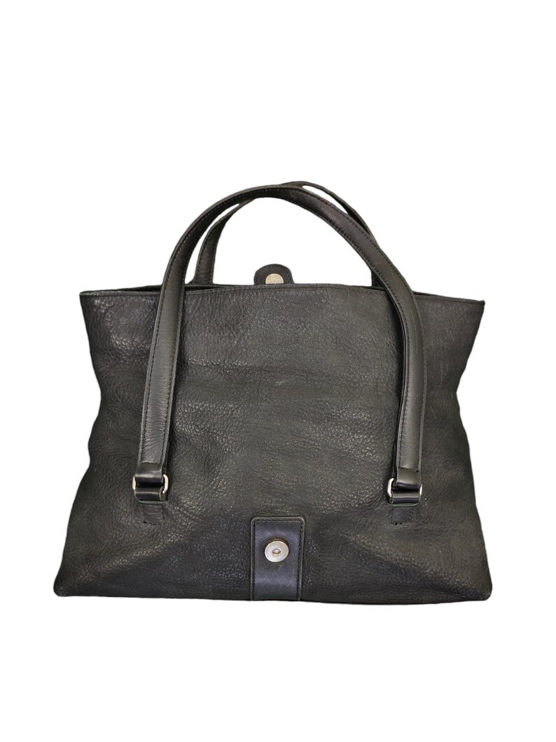 May include: A black leather tote bag with two top handles and a single snap closure.