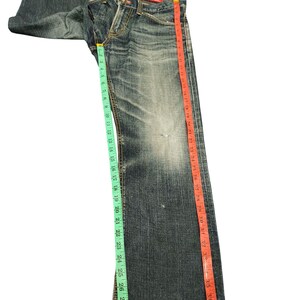 May include: Faded blue denim jeans with a straight leg cut. The jeans are measured with a green and red measuring tape. The inseam measures approximately 30 inches.