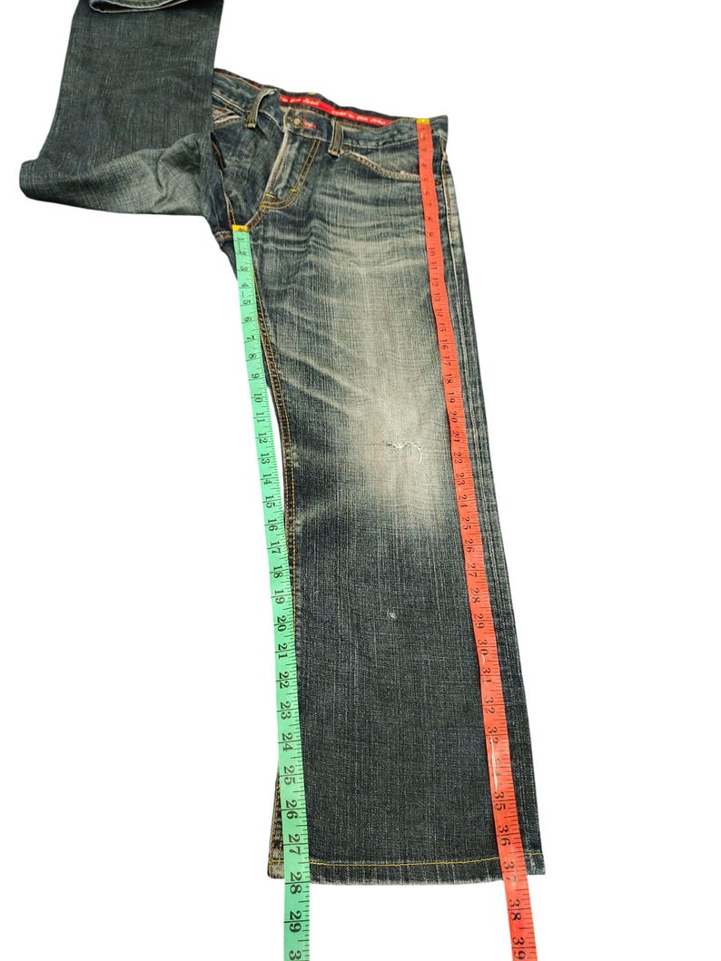 May include: Faded blue denim jeans with a straight leg cut. The jeans are measured with a green and red measuring tape. The inseam measures approximately 30 inches.
