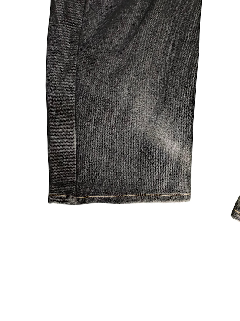 Op de afbeelding: Close-up van een donkergrijze spijkerbroek. De jeans heeft een vervaagde uitstraling met zichtbare stiksels langs de zoom. De stof heeft een textuur en de algehele stijl is casual.