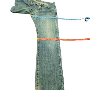 May include: Light blue denim jeans with a classic five-pocket design. The jeans are laid flat with measuring tapes across the waist, thigh, and length. The jeans are approximately 30 inches long.
