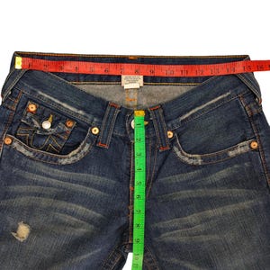 K&ouml;nnte beinhalten: Blaue Jeans aus Denim mit einem roten und wei&szlig;en True Religion-Etikett und einem gr&uuml;nen Ma&szlig;band. Das Band misst 38 cm.