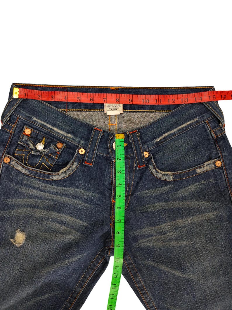 K&ouml;nnte beinhalten: Blaue Jeans aus Denim mit einem roten und wei&szlig;en True Religion-Etikett und einem gr&uuml;nen Ma&szlig;band. Das Band misst 38 cm.