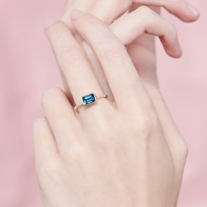 May include: A gold ring with a blue gemstone set in a square shape.