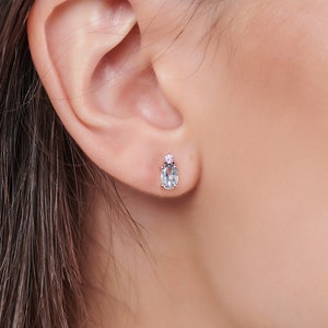A unique stud earring in yellow gold with a light sky blue topaz gemstone and a round white natural diamond worn by a model.