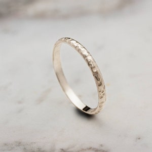 A yellow gold ring with a hammered surface on the outer part and a pished on the inside is laid beautifully shown on a marble surface.