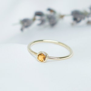 May include: A delicate gold ring with a small, round, orange gemstone.