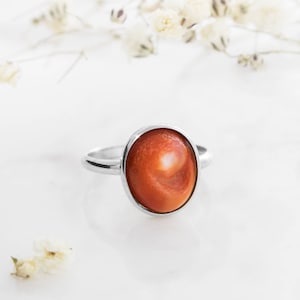 May include: A silver ring with an oval-shaped orange and white gemstone.