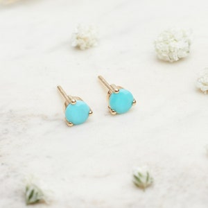 May include: A pair of gold stud earrings with turquoise stones. The earrings are small and delicate, and they would make a great gift for a friend or loved one.