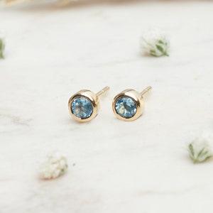 May include: A pair of gold stud earrings with small, round, light blue gemstones.