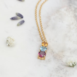 May include: A gold chain necklace with a pendant featuring three round gemstones: a red garnet, a blue topaz, and a yellow citrine.
