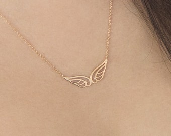 May include: A delicate gold necklace with a small, openwork angel wing pendant. The necklace is worn by a person with long brown hair.