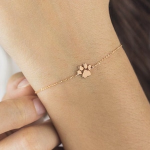 A high-quality charm bracelet with a tiny paw with a distinct separation between the pads and an adjustable chain in rose gold worn by a model.