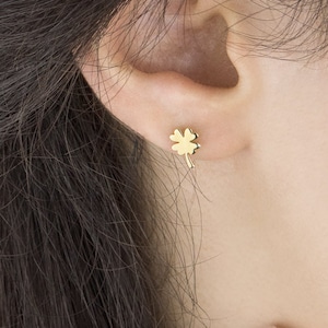 以下が含まれることがあります： 四つ葉のクローバーの小さな金のスタッドイヤリングをつけた人の耳のクローズアップ。