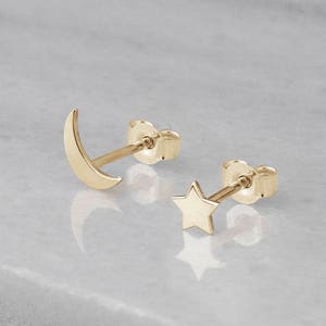 May include: A pair of gold earrings featuring a crescent moon and a star design. The earrings are small and delicate, perfect for everyday wear.