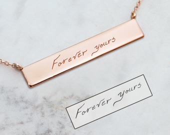 May include: A rose gold necklace featuring a delicate chain and a rectangular pendant engraved with the words "Forever Yours" in cursive handwriting.
