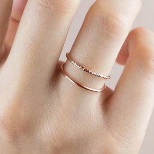 May include: Two thin rose gold rings on a finger. The top ring has a textured surface and the bottom ring is smooth.