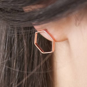 A thin hexagon-shaped stud earring in rose gold and with a push-back closure is shown worn by a model.