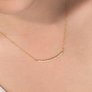 A minimalist style yellow gold necklace with a thin cable chain and a curved bar with natural white diamonds embedded on it worn by a model.