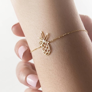 Puede incluir: Un brazalete de oro con un dije de piña. El brazalete es delicado y presenta una cadena simple con un dije de piña.