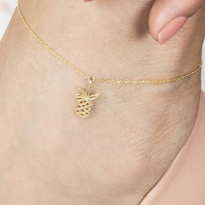May include: Gold pineapple ankle bracelet with a delicate chain. The charm is a detailed pineapple design with a small diamond in the centre.