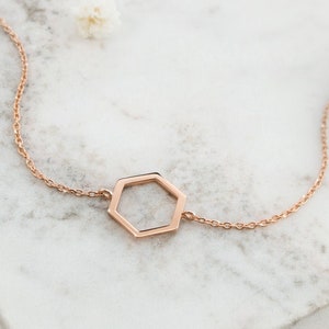 May include: A delicate rose gold necklace with a geometric hexagon pendant. The chain is a simple, fine link style.
