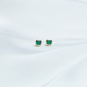 A Beautiful set of yellow gold stud earrings with a tiny round green agate gemstone laid down on a white sheet.