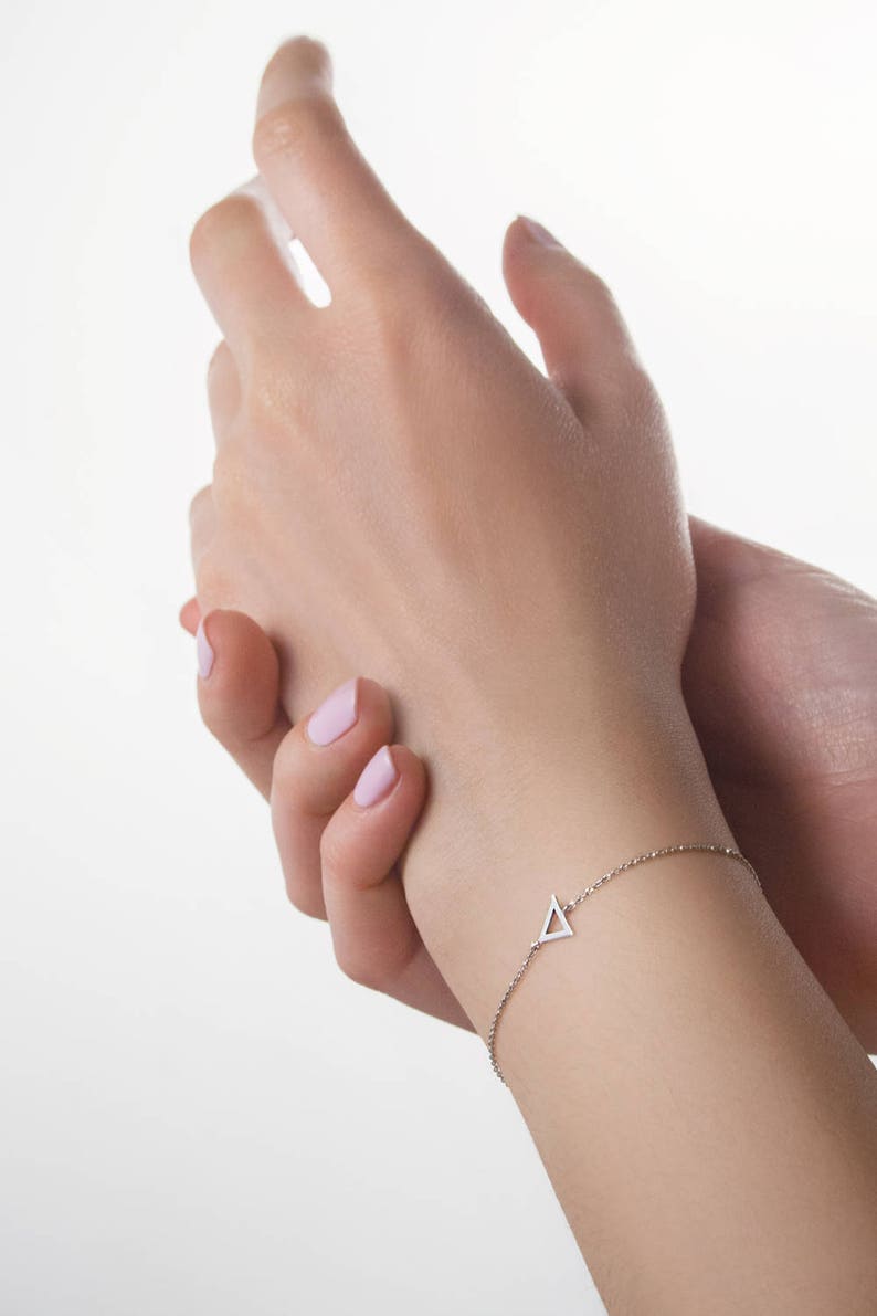 A hand-crafted bracelet soldered to a triangle frame charm in white gold. A minimalist style piece with an adjustable chain laid worn by a model.