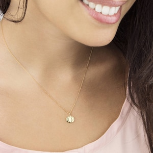 A yellow gold pendant necklace with a pumpkin charm with engraved details is shown worn by a model.
