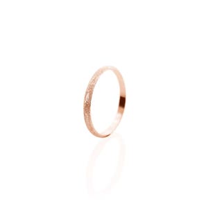May include: A thin rose gold band ring with a textured finish.