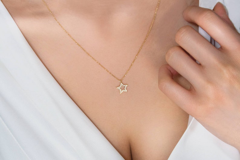 Worn by a model, a yellow gold necklace with a special star outline charm and natural white diamonds embedded in it.