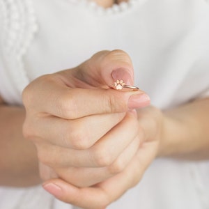 Puede incluir: Un anillo de oro rosa con un dise&ntilde;o de huella de pata. El anillo est&aacute; siendo sostenido por una mano con u&ntilde;as cuidadas.