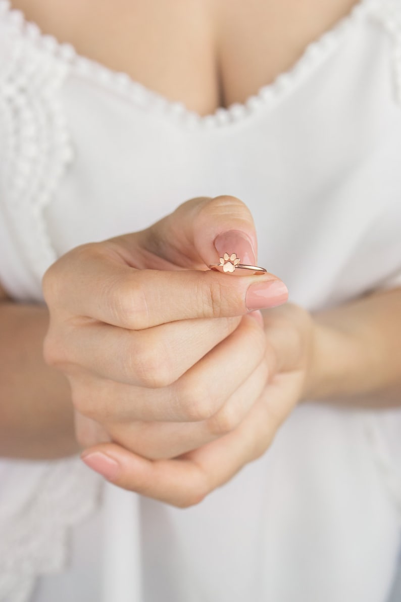 Puede incluir: Un anillo de oro rosa con un dise&ntilde;o de huella de pata. El anillo est&aacute; siendo sostenido por una mano con u&ntilde;as cuidadas.
