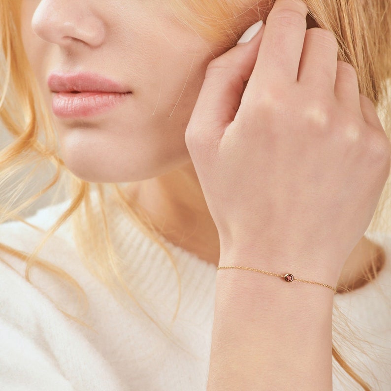 A special bracelet with a deep red garnet gemstone and an adjustable chain in yellow gold worn by a model.