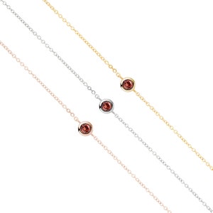 All three color options of the solid gold bracelet with a deep red garnet gemstone and an adjustable chain. Rose, white and yellow gold, every option displayed right next to each other on a white background.
