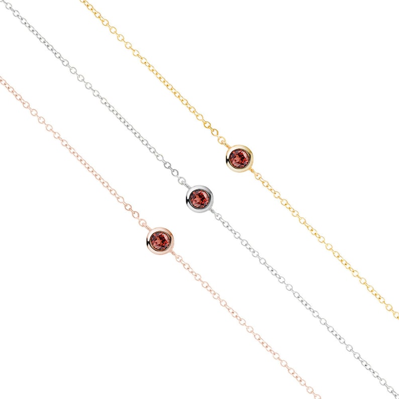 All three color options of the solid gold bracelet with a deep red garnet gemstone and an adjustable chain. Rose, white and yellow gold, every option displayed right next to each other on a white background.