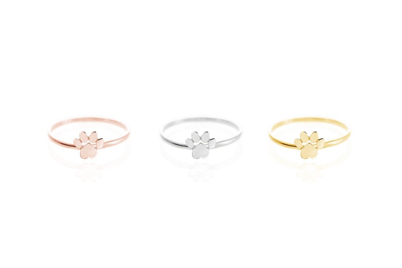 All three color options of the paw print band ring in yellow, white, and rose gold, every option displayed right next to each other on a white background.