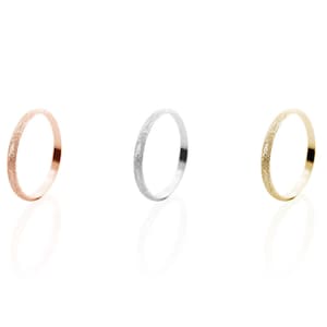 All three color options of the solid gold band ring with a sandstone finish. Rose, white and yellow gold, every option displayed right next to each other on a white background.