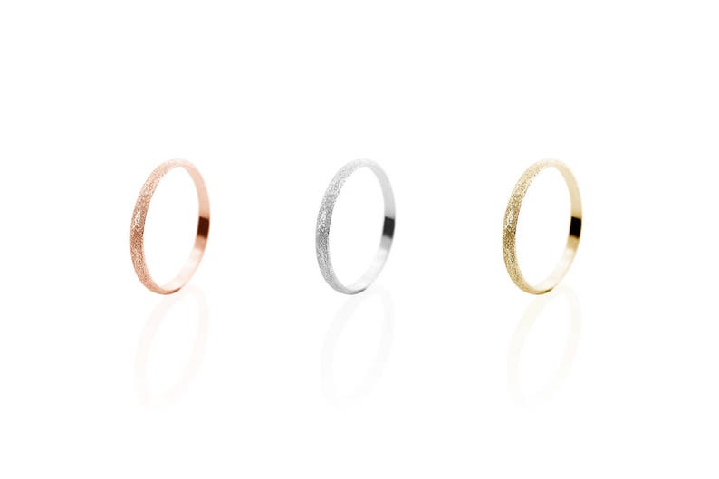 All three color options of the solid gold band ring with a sandstone finish. Rose, white and yellow gold, every option displayed right next to each other on a white background.