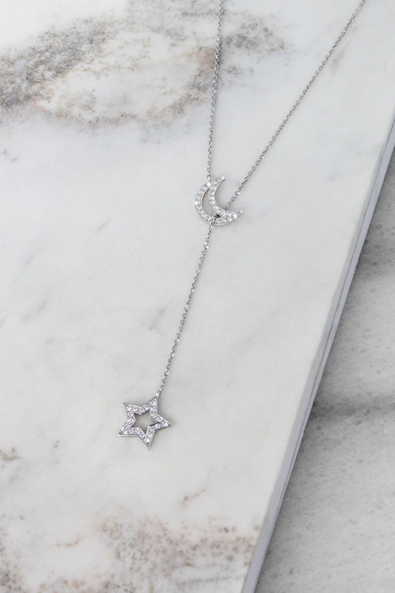 Beautifully shown on a marble display piece, is a special sparkling lariat necklace with two of the most popular outline chams. Both the crescent moon and a star are covered in natural white diamonds in white gold.