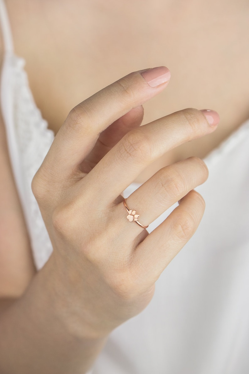 A high-quality band ring with a tiny paw print with a distinct separation between the pads in rose gold worn by a model.