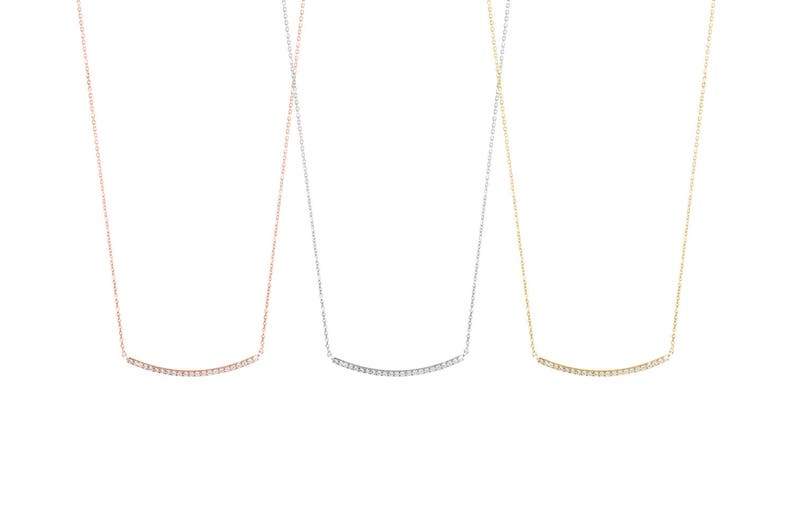 All three color options of the solid gold necklace with a thin cable chain and a curved diamond bar. Rose, white and yellow gold, every option displayed right next to each other on a white background.