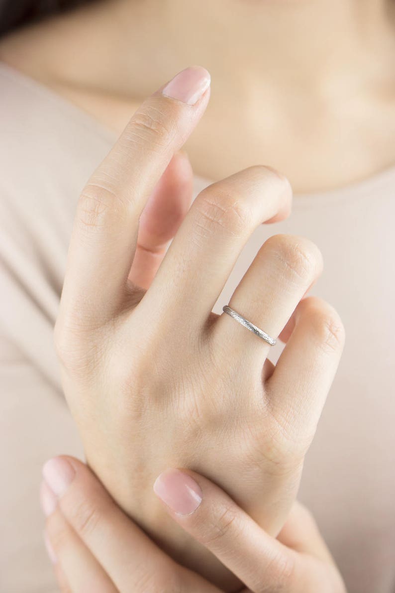 A classic and unique white gold band ring with a sandstone finish worn by a model's hand.