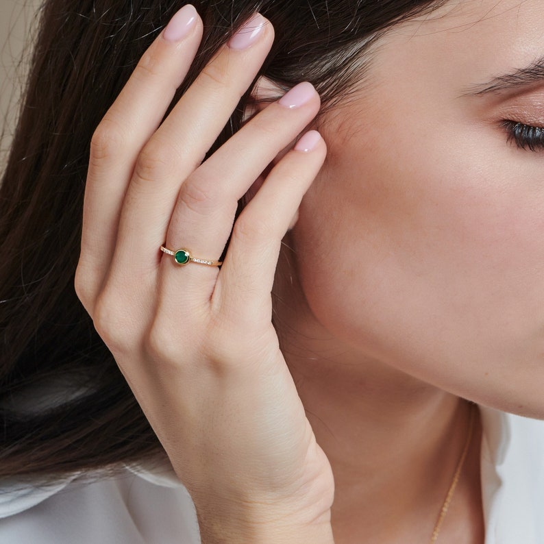 Worn by a model, a beautiful yellow gold ring with a round-shaped green agate gemstone and five tiny diamonds on each side of the stone, around its band.