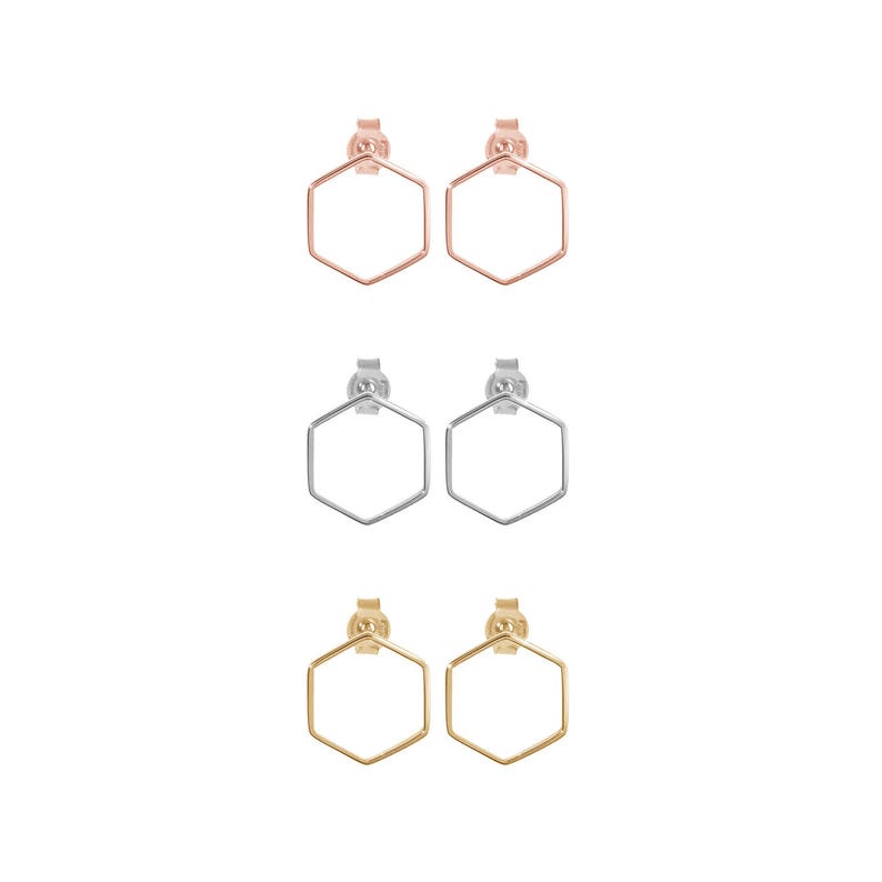 All three color options of the solid gold pair of thin hexagon-shaped stud earrings and with a push-back closure. Rose, white and yellow gold, every option displayed right next to each other on a white background.