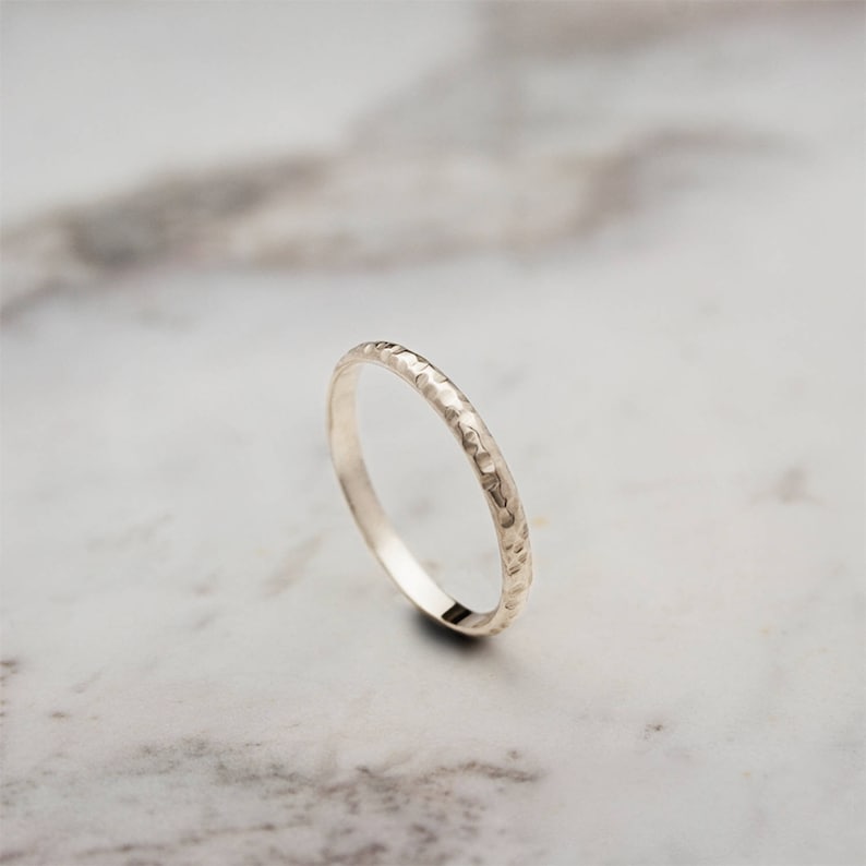 A yellow gold ring with a hammered surface on the outer part and a pished on the inside is laid beautifully shown on a marble surface.