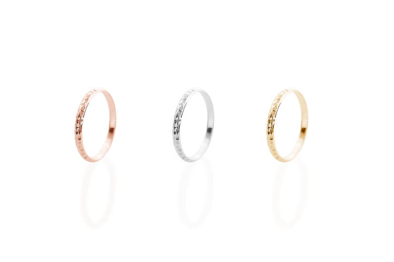All three color options of the solid gold ring with a hammered surface on the outer part and a pished on the inside. Rose, white and yellow gold, every option displayed right next to each other on a white background.