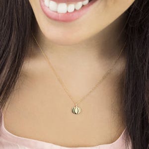 Op de afbeelding: Een gouden ketting met een klein, geel pompoen hanger.