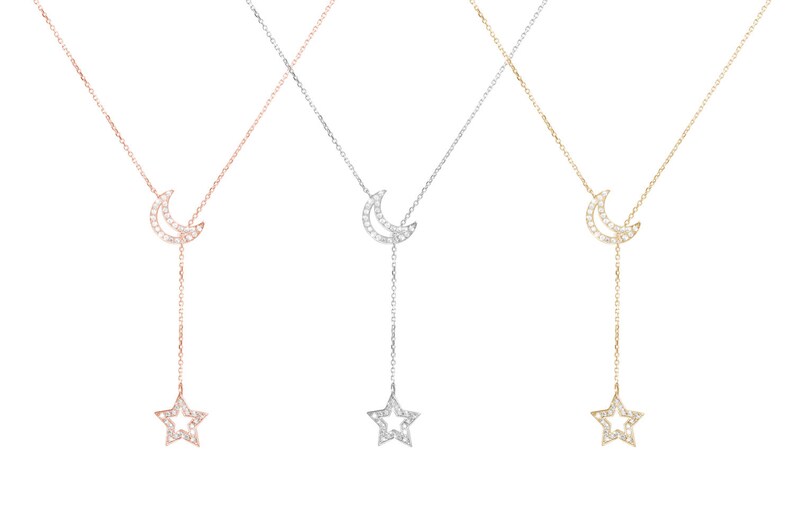 All three color options of the solid gold lariat necklace with two outline chams. A crescent moon and a star are both covered in natural white diamonds. Rose, white and yellow gold, every option displayed on a white background.